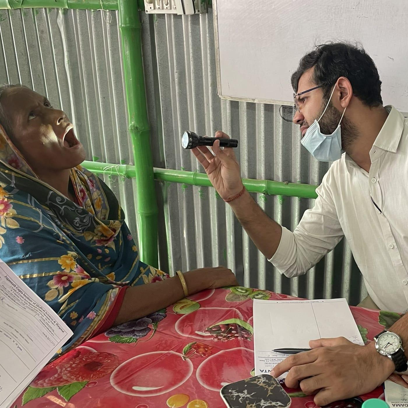 A Krancer doctor in a mask examining a patient's mouth with a torch at a community screening camp