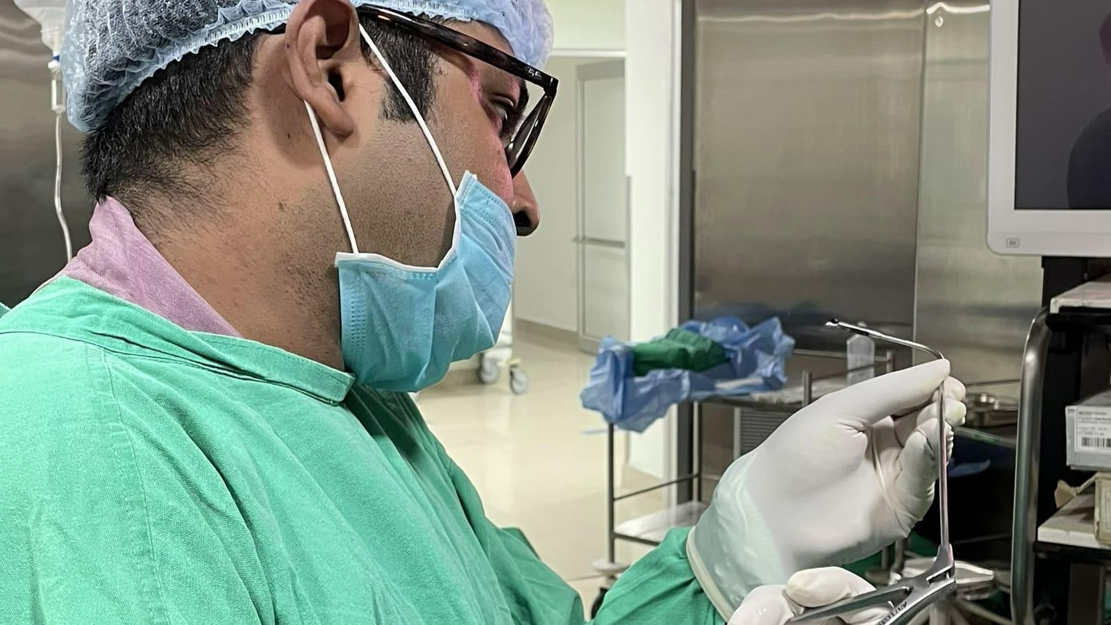 A Krancer ENT surgeon in scrubs and a mask holding a surgical instrument
